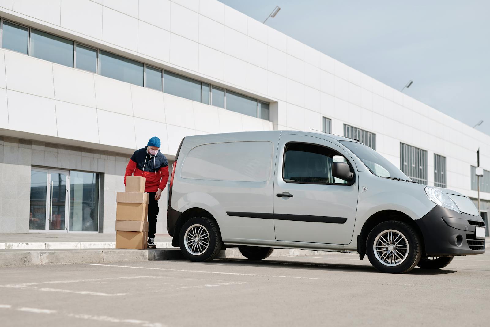 commerical auto, delivery driver wearing a face mask unloads packages from a van outside a modern building.